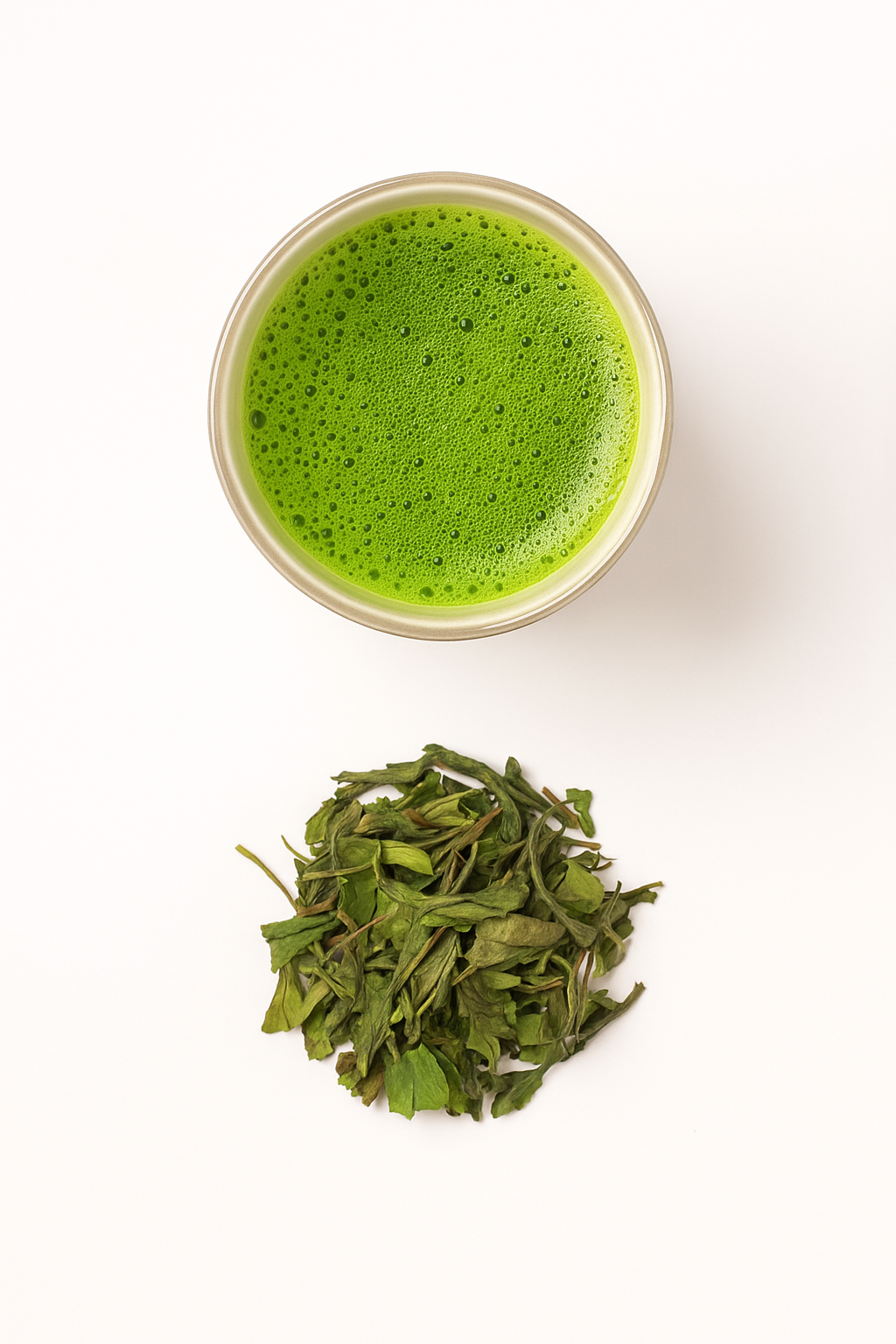 Overhead view of a bowl of frothy whisked matcha above a pile of loose green tea leaves, drink and raw ingredient