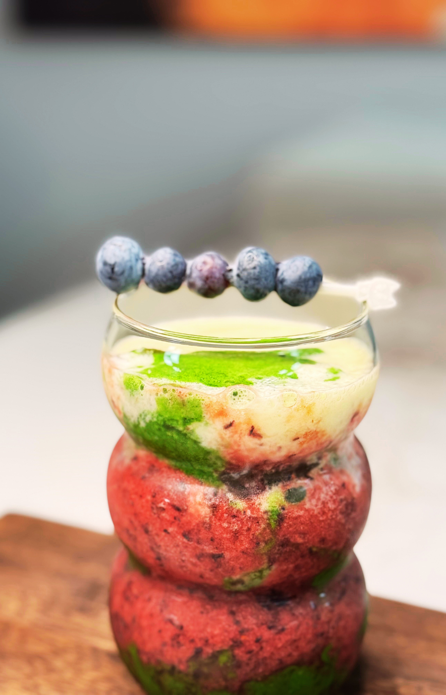 Matcha blueberry smoothie in a ribbed glass layered with berries and blueberries threaded on a skewer