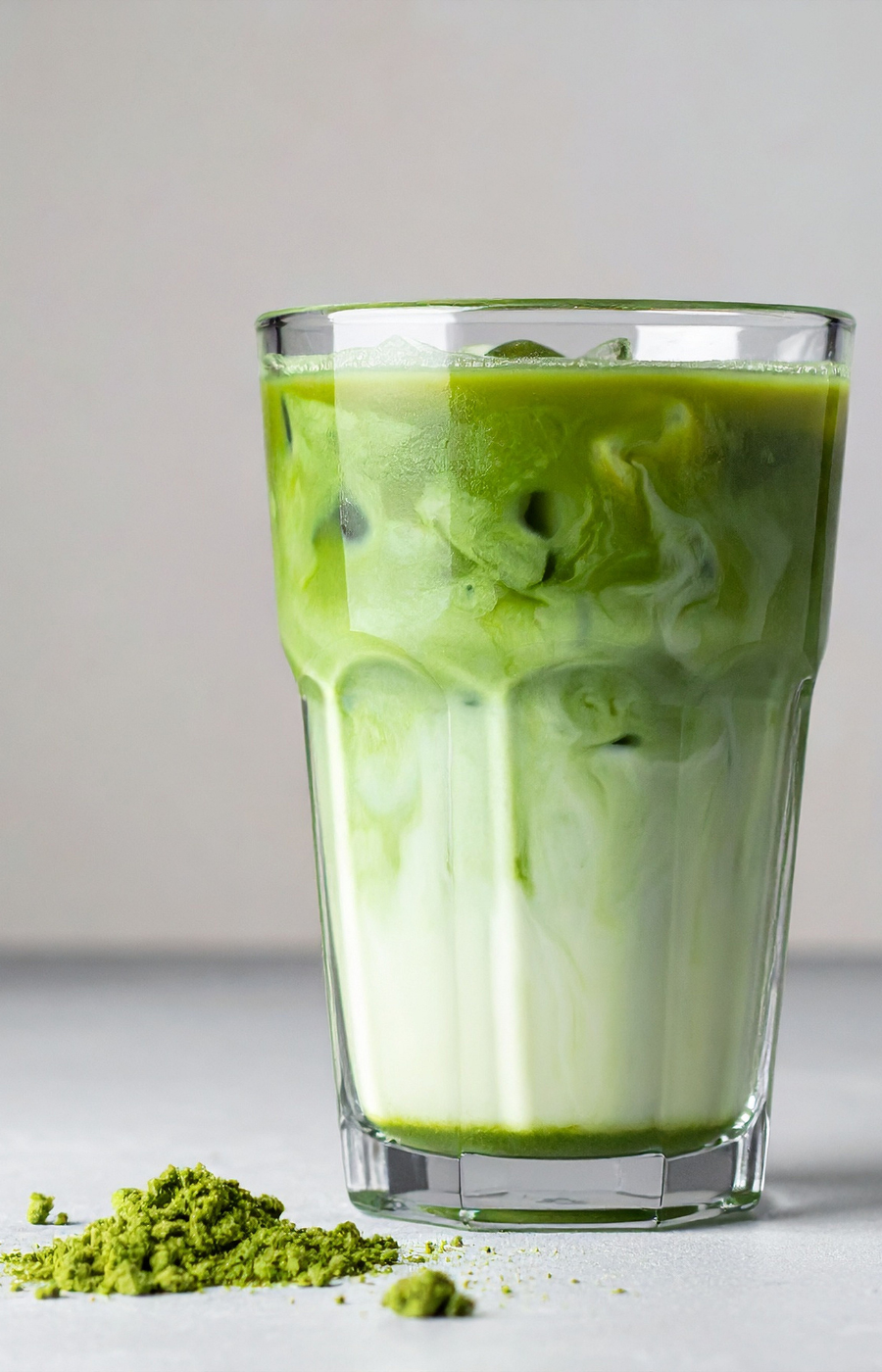 Nippon Matcha iced latte in a ribbed glass beside a pile of organic matcha powder, ceremonial grade close-up