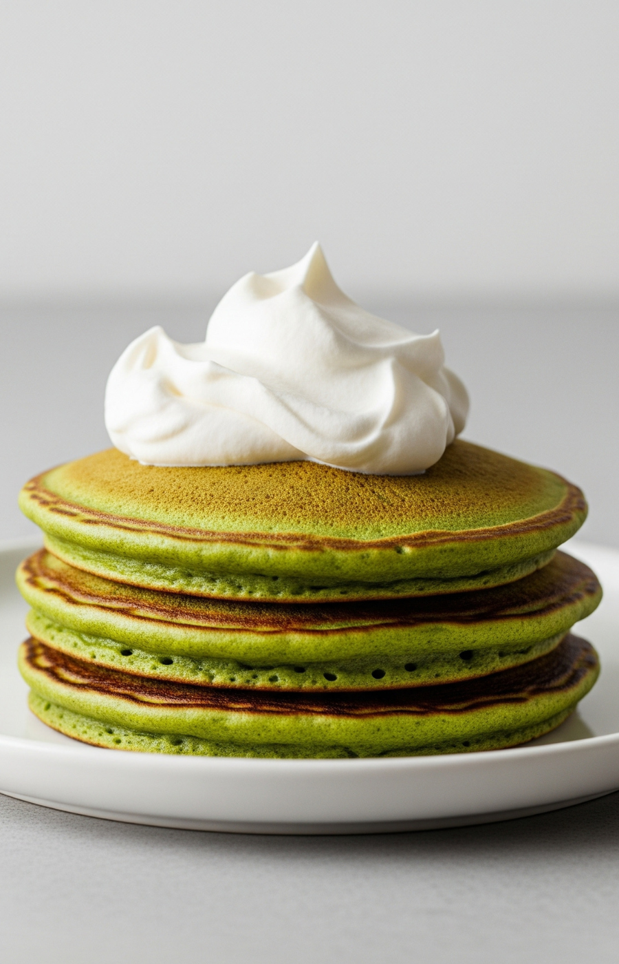 Stack of four Nippon Matcha pancakes topped with whipped cream on a white plate, minimal breakfast styling
