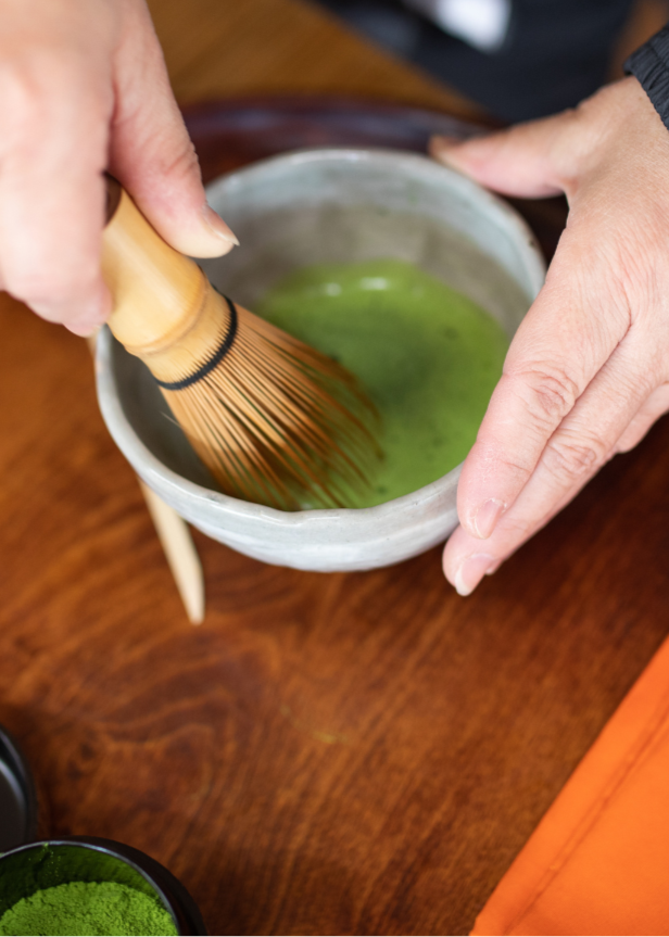 Person stirring matcha green tea in a small bowl with a whisk on a wooden surface.