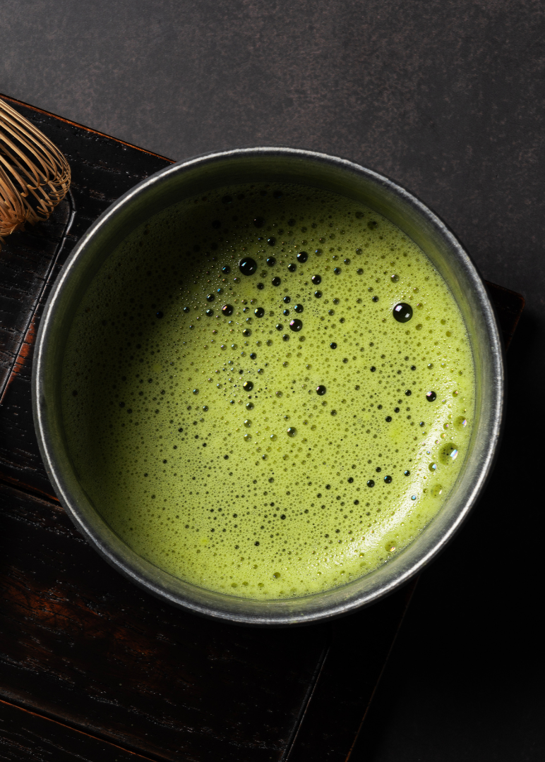 Matcha green tea powder and a bowl of matcha tea on a dark surface.